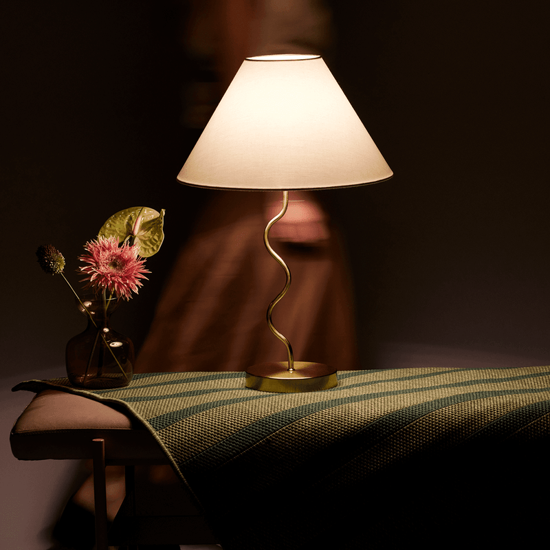 Elegant modern lamp with a curved base next to decorative flowers on a table.