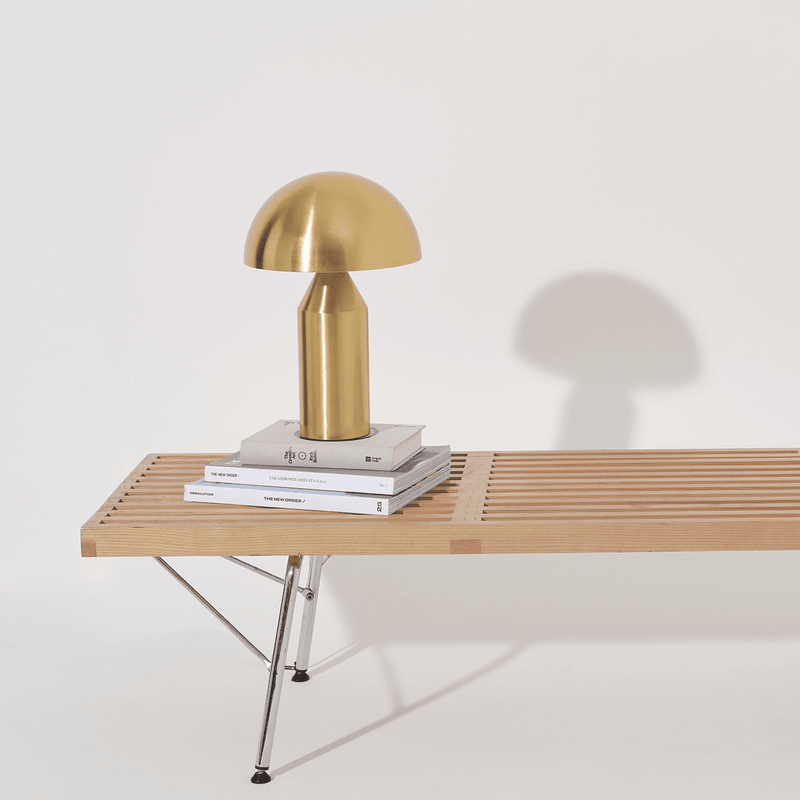 Golden table lamp on a wooden bench with books, minimalistic home decor.
