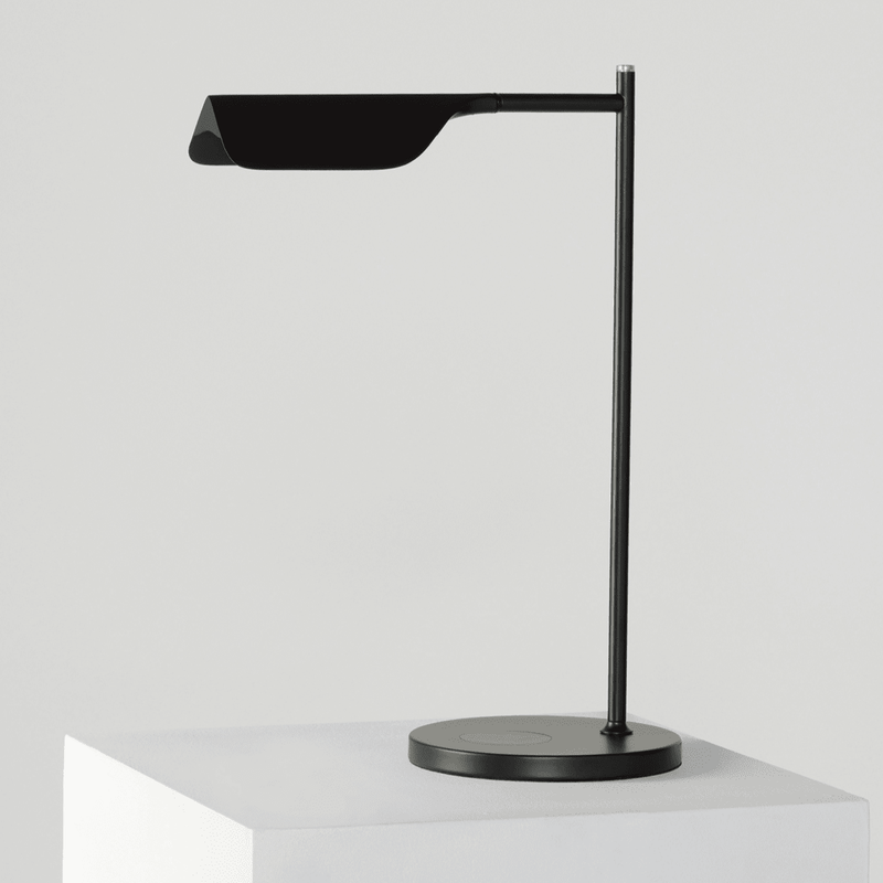 Modern black minimalist desk lamp on a white pedestal, showcasing sleek design and adjustable features for optimal workspace lighting.