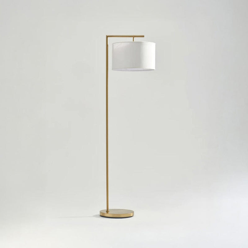 Modern gold floor lamp with white drum shade on minimalist background.