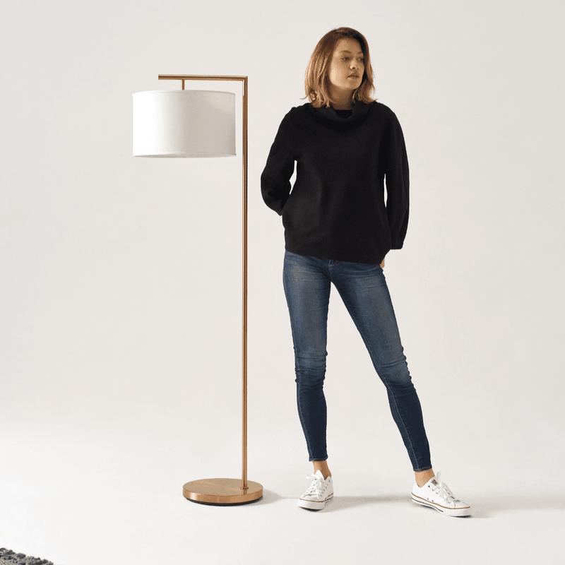 Woman in casual outfit standing beside modern floor lamp in minimalist interior.