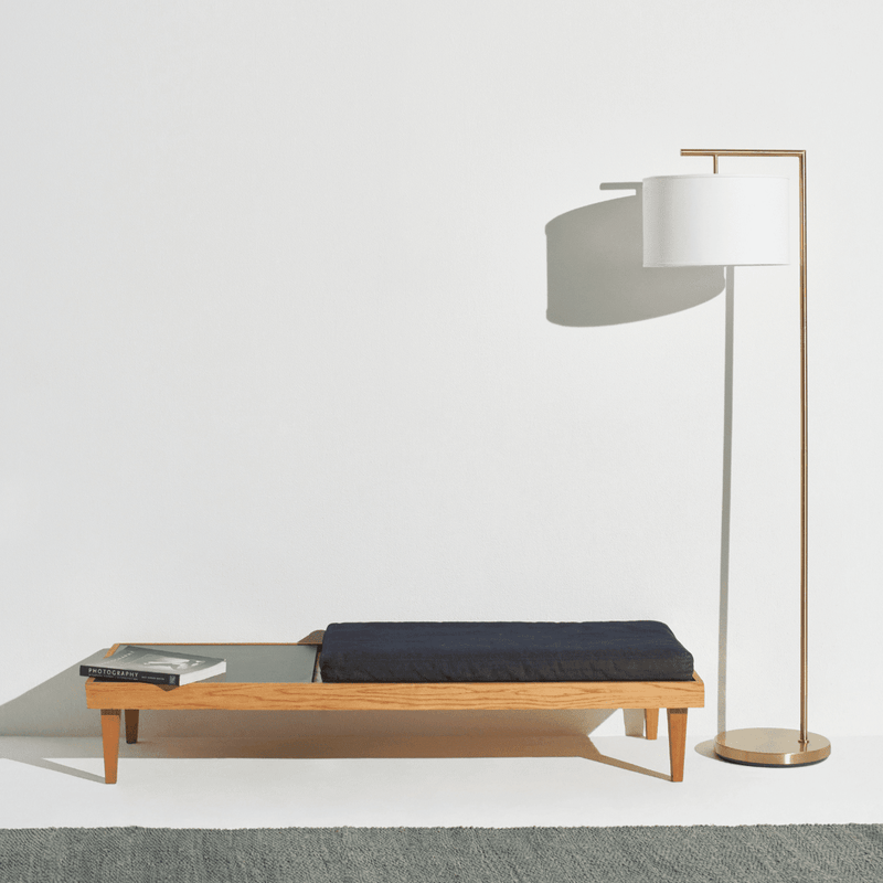 Modern wooden bench with black cushion beside a contemporary floor lamp.