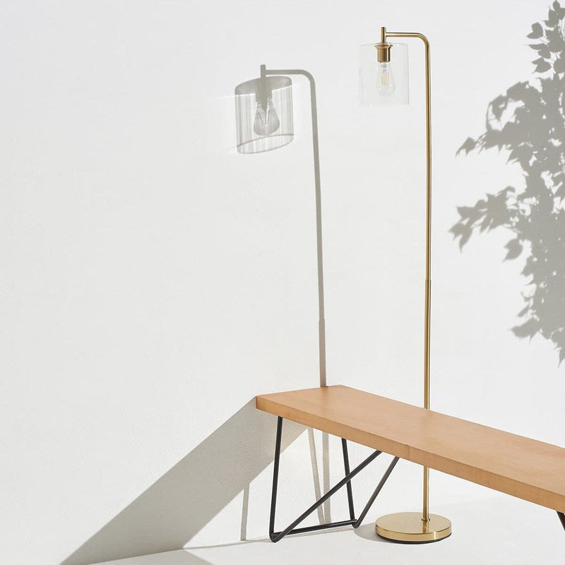 Modern gold floor lamp casting shadow on minimalist wooden bench against white wall.