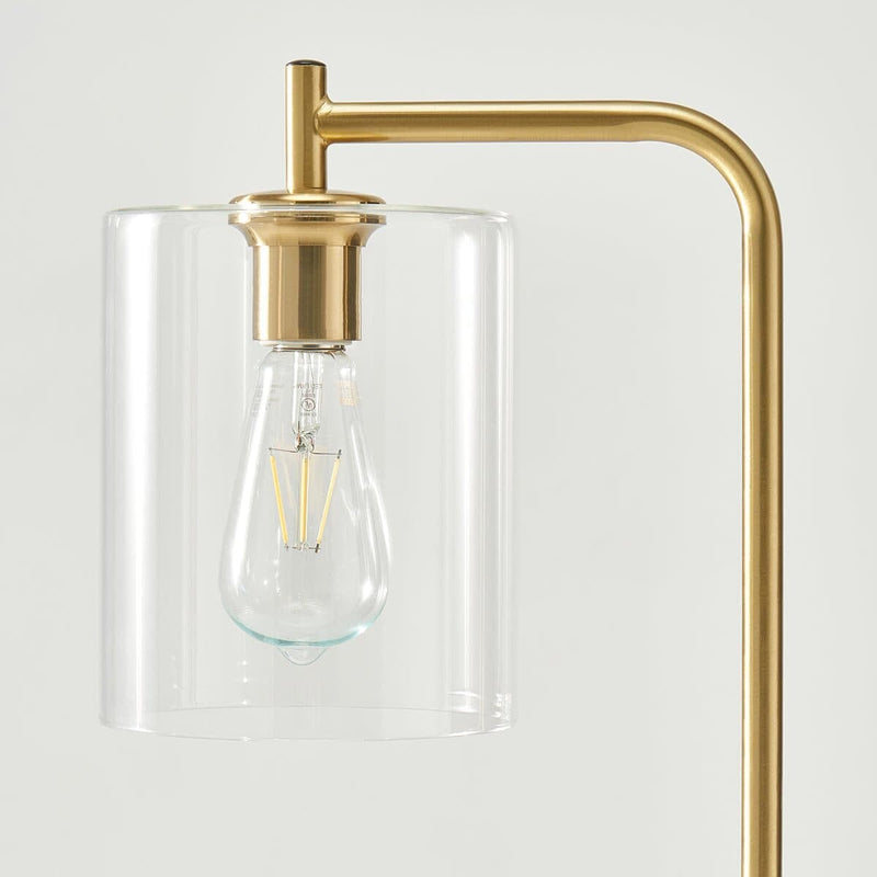 Gold modern lamp with transparent glass shade and visible vintage-style bulb.