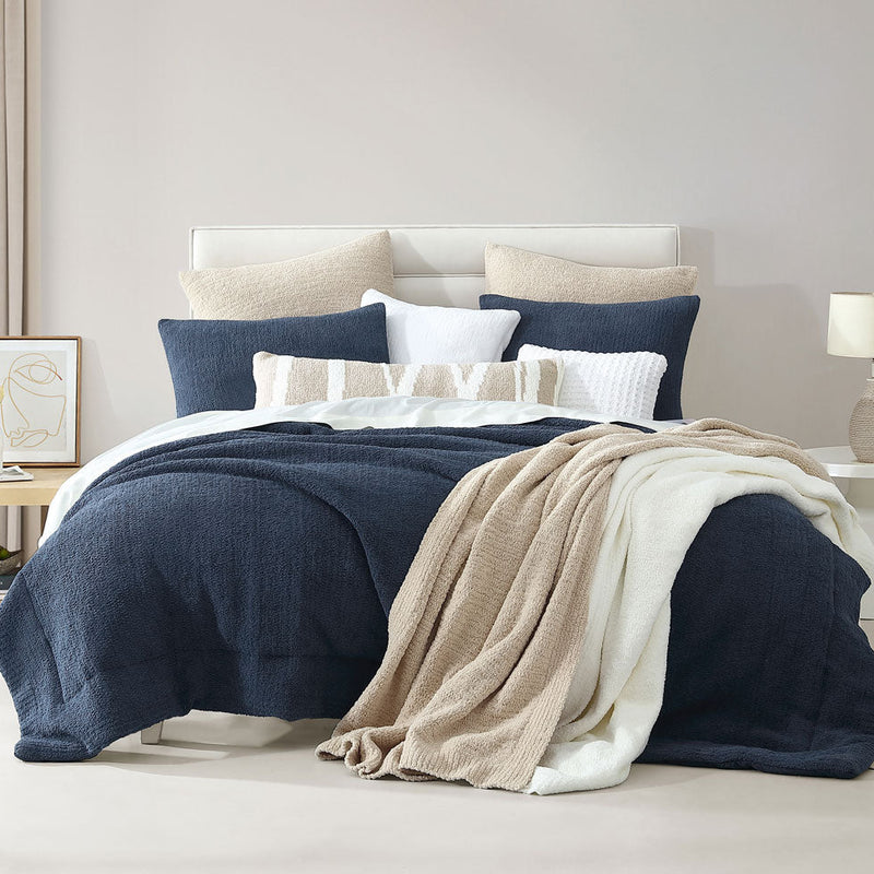 Luxurious navy and beige bedding set with plush pillows and cozy throws in a modern bedroom.