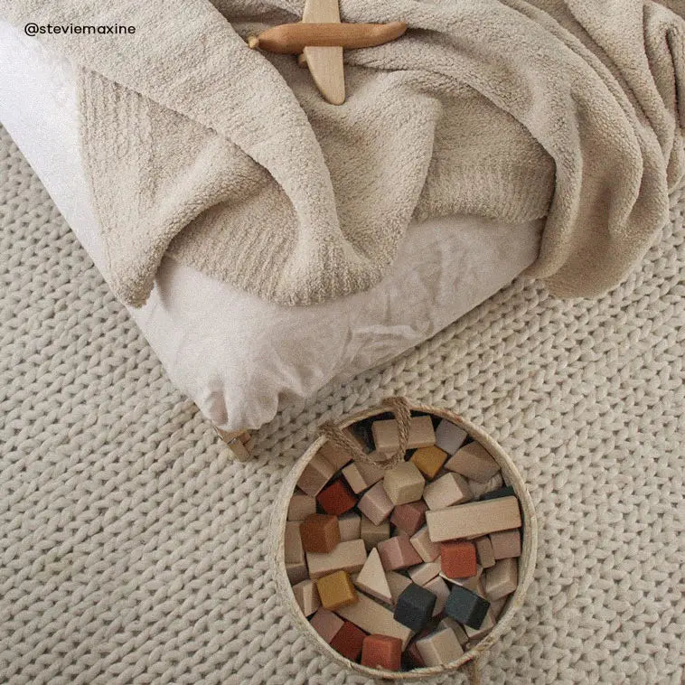 Cozy beige bedding set with wooden blocks on woven rug in serene neutral nursery decor.