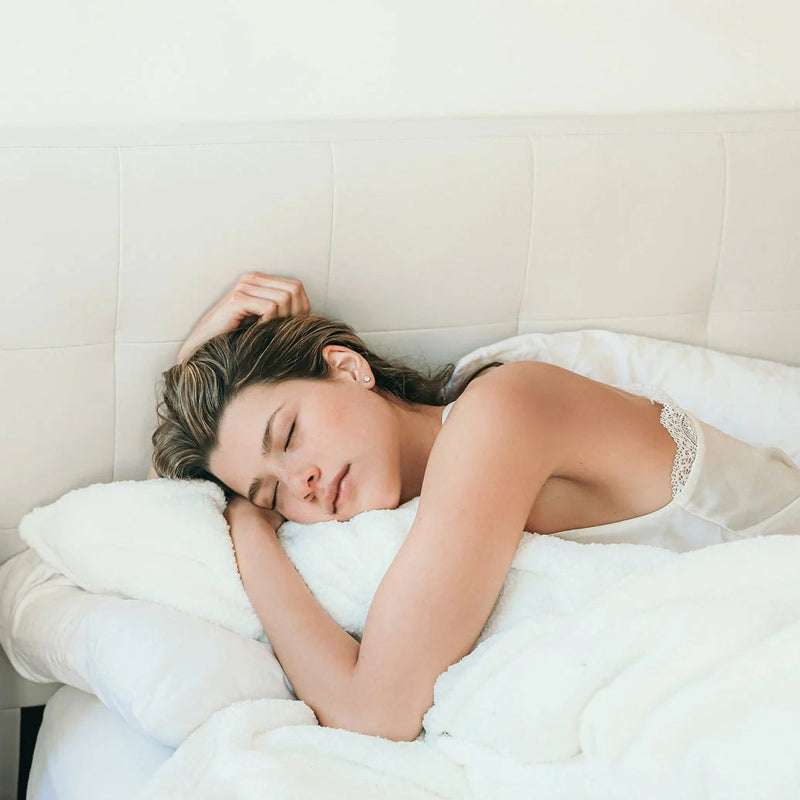 Woman sleeping peacefully in bed with white sheets.