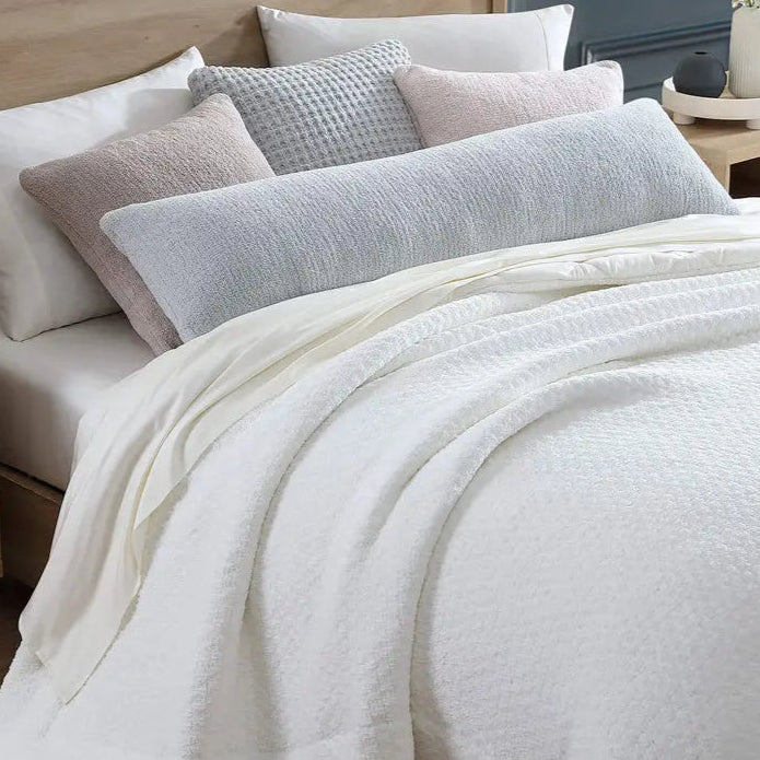 Luxurious white bedspread with soft textured pillows on a modern wooden bed for a cozy bedroom atmosphere.
