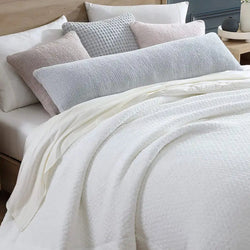 Luxurious white bedspread with soft textured pillows on a modern wooden bed for a cozy bedroom atmosphere.