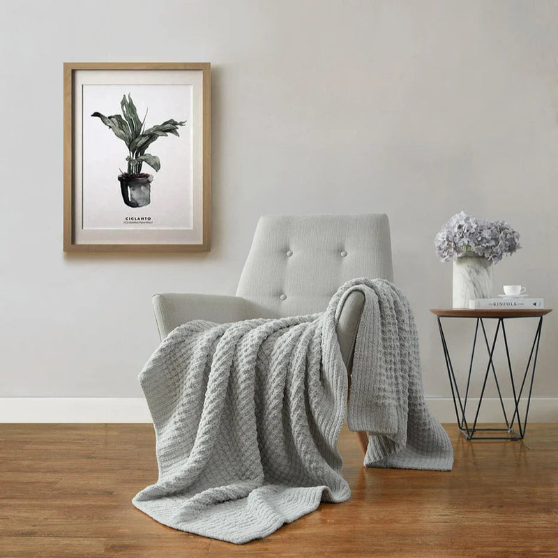 Cozy living room with gray armchair, gray throw blanket, framed botanical art, and rustic side table.