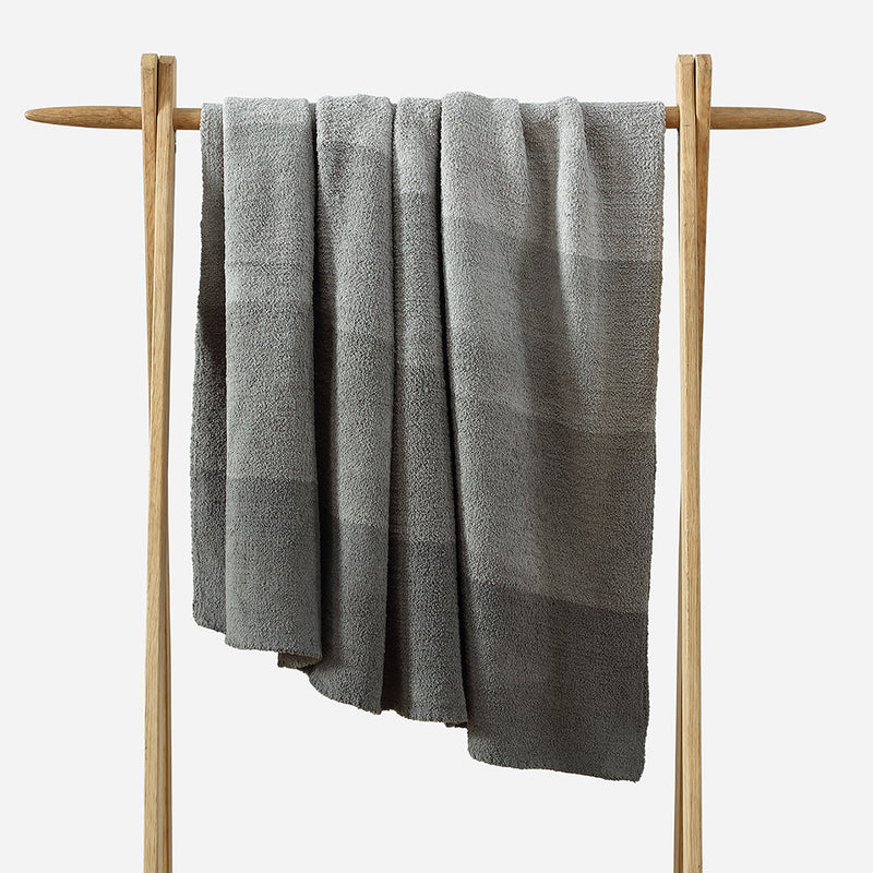 Luxurious gray towel draped over a wooden towel rack in a minimalist bathroom setting.