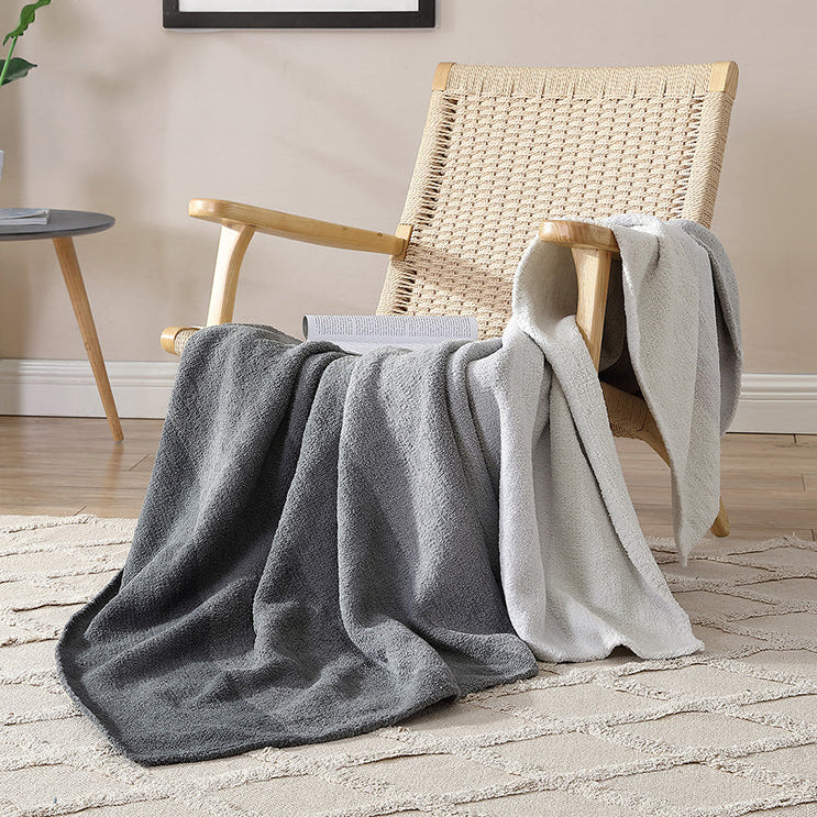 Woven chair with cozy gray and white throw blankets in a modern living room setting.