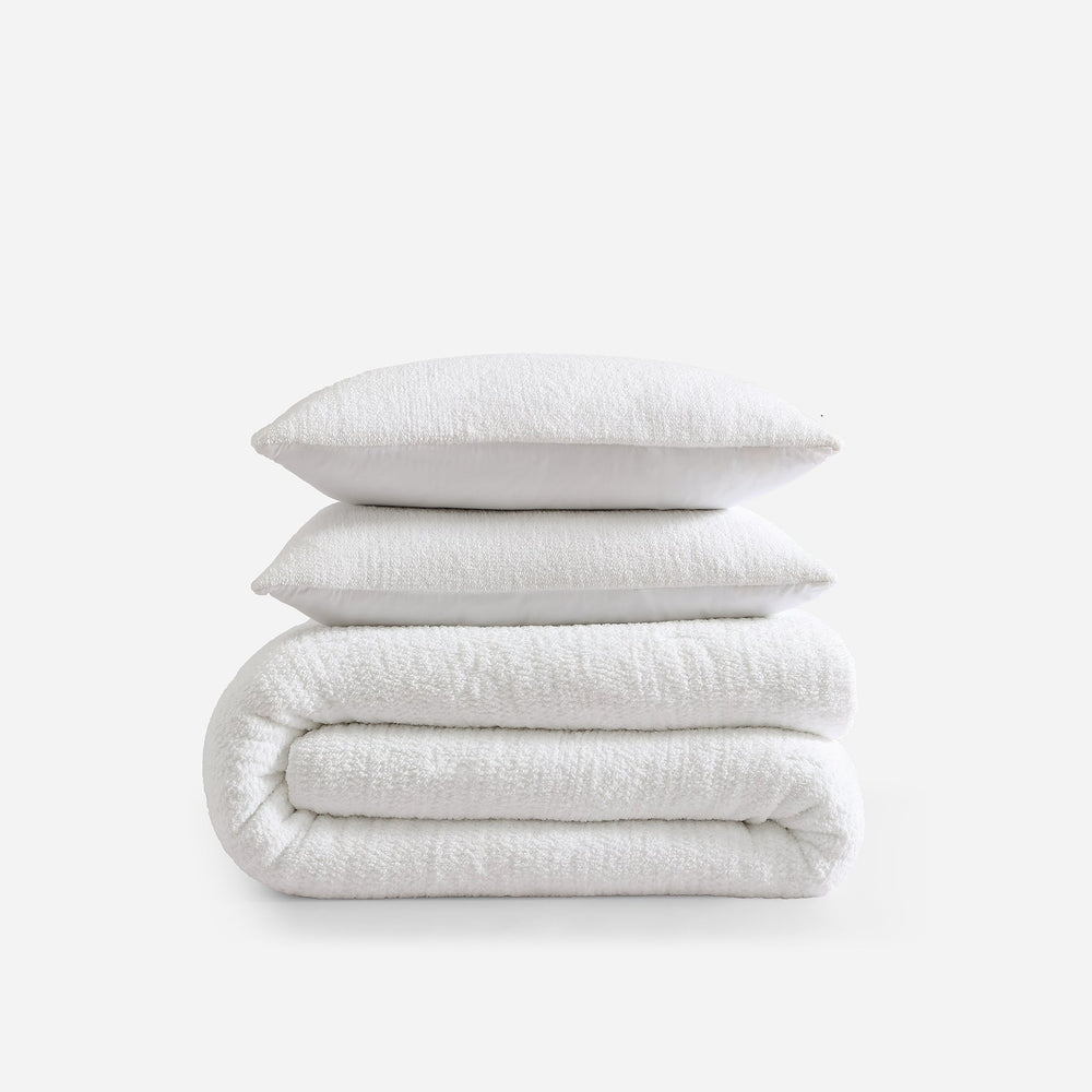 Luxury white comforter and pillows set on a white background for all-season bedding.