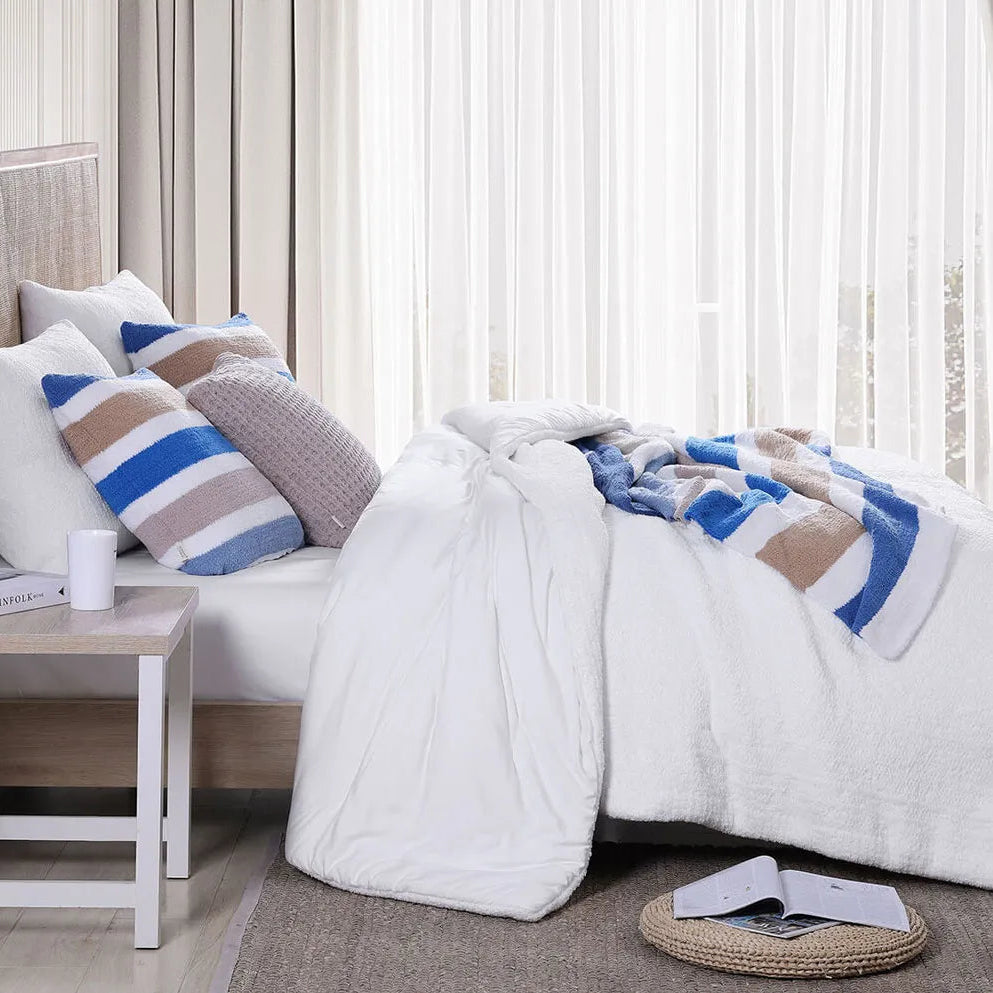 Cozy bedroom interior with white bedding, striped pillows, and natural light from sheer curtains.