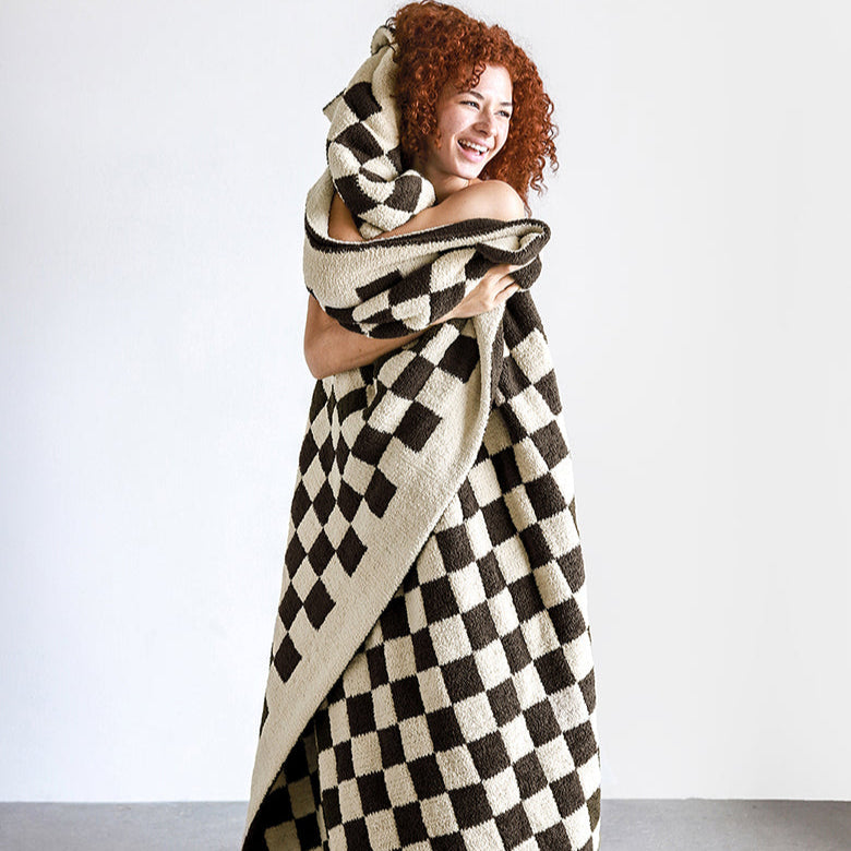 Smiling woman wrapped in a cozy checkered blanket, home comfort and style.