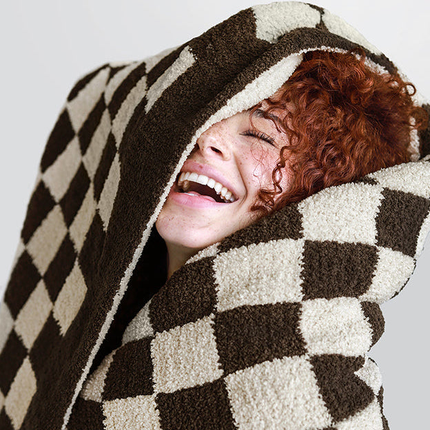Person smiling wrapped in a cozy checkered blanket.
