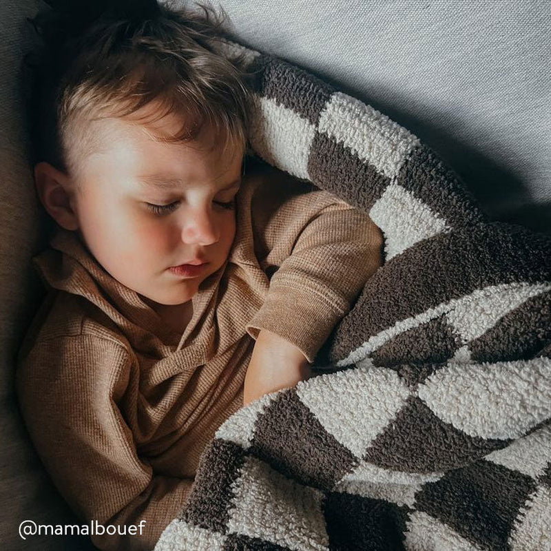 Sleeping toddler wrapped in a cozy checkered blanket on a couch.