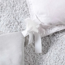 Close-up of a white and gray fleece blanket with ribbon tie on soft carpet background.