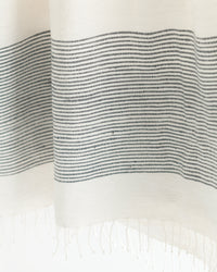 Close-up of white fabric with black horizontal stripes and fringed edge.