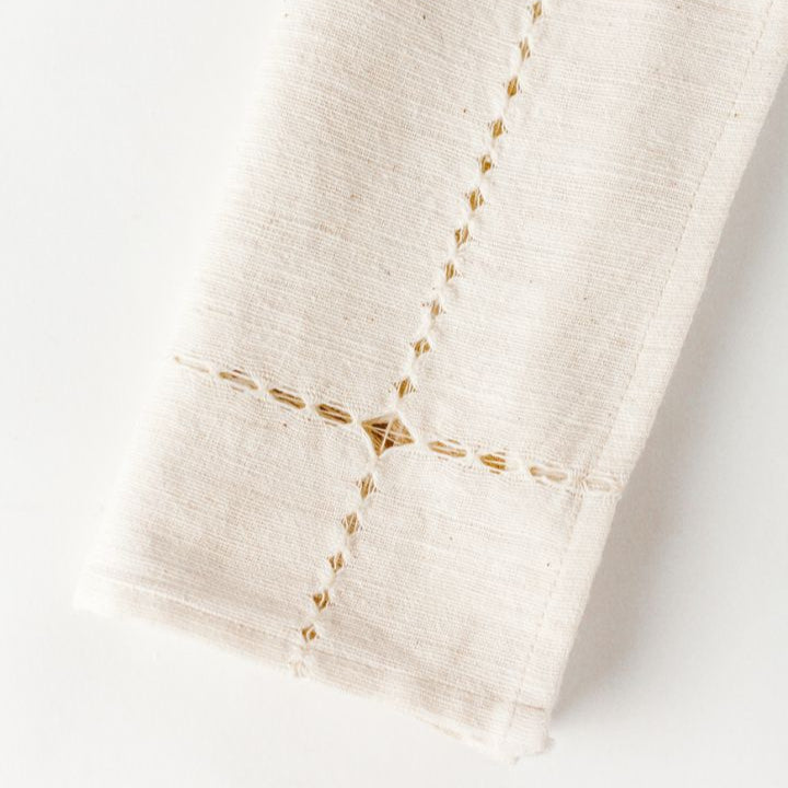 Handwoven white linen napkin with intricate hemstitch detail.