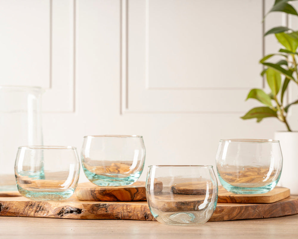 Four elegant clear glass cups on a wooden tray in a modern kitchen setting.