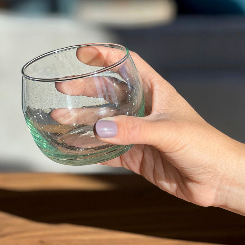 Hand holding an empty transparent glass with a natural light background.