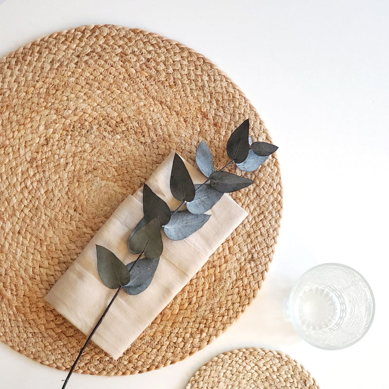 Elegant table setting with a natural woven placemat, neutral napkin, and eucalyptus branch.