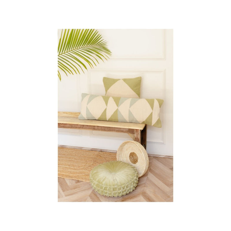 Decorative throw pillows and cushions on a wooden bench with a tropical leaf accent against a minimalist white wall.