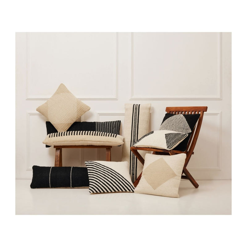 Modern farmhouse aesthetic with black and beige geometric patterned throw pillows on wooden chairs against a white wall.