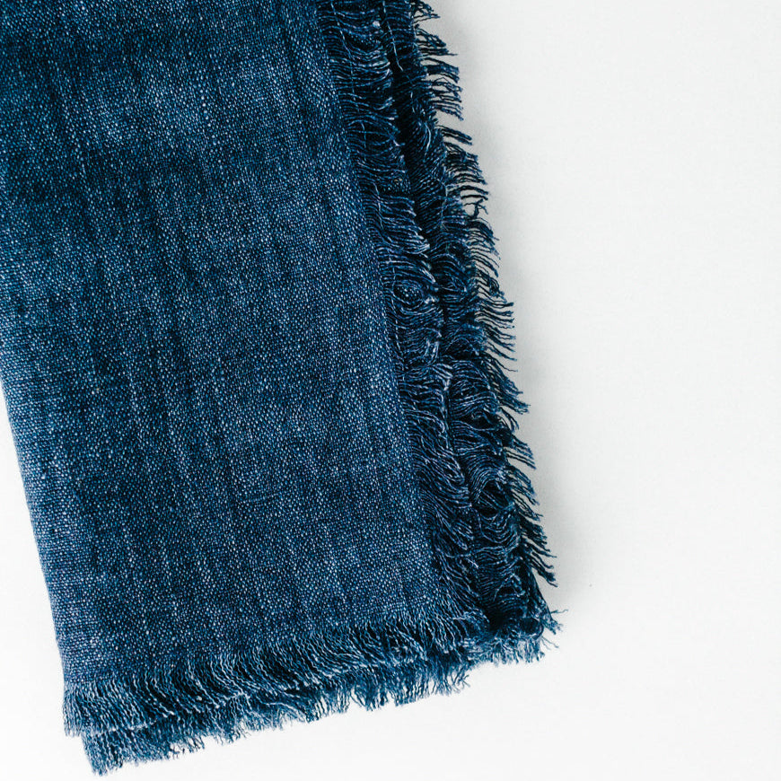 Close-up of blue denim fabric with frayed edges, highlighting texture and design details.