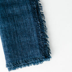 Close-up of blue denim fabric with frayed edges, highlighting texture and design details.