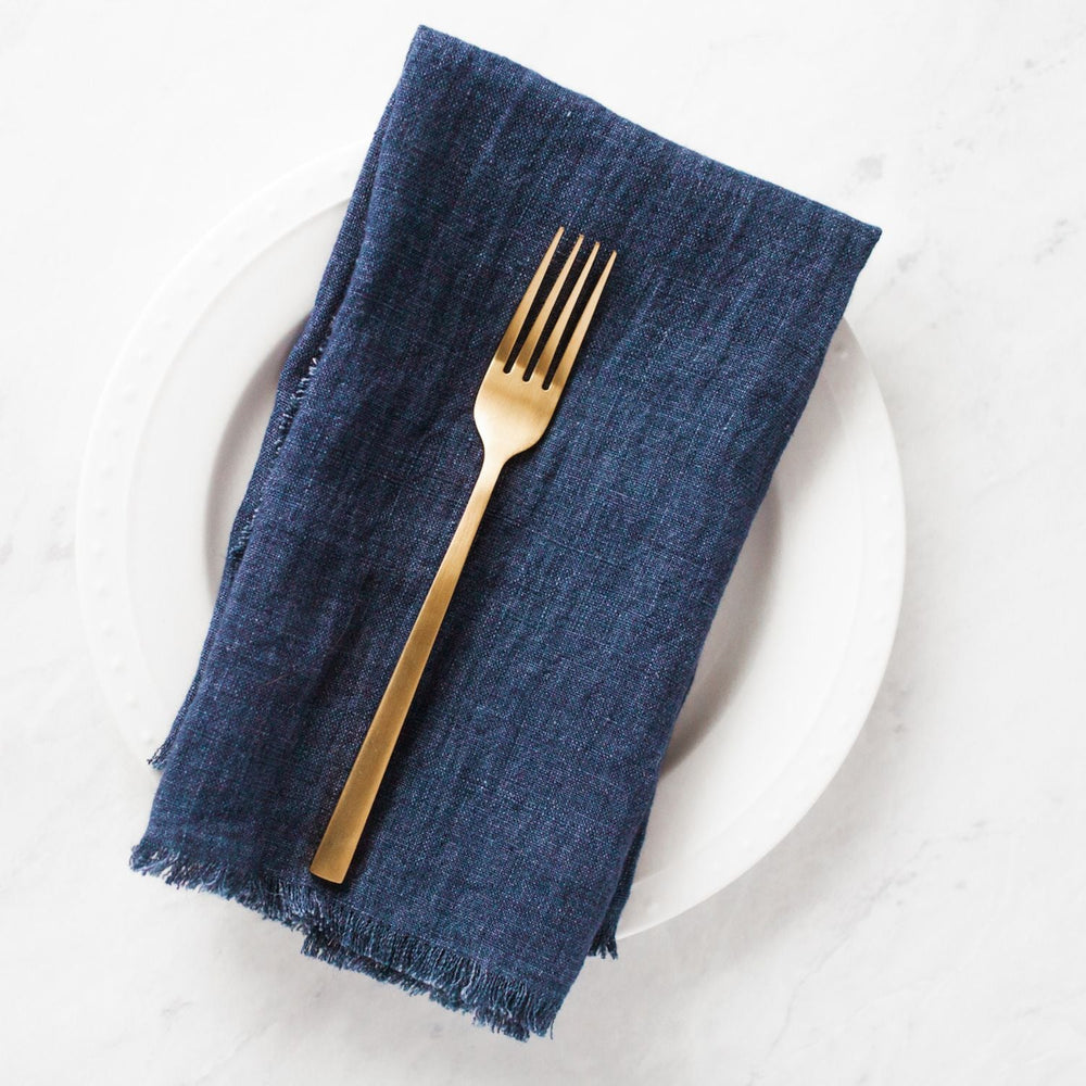 Gold fork on dark blue napkin atop a white plate, flat lay table setting.