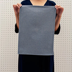Person holding a large grey textured fabric swatch against a pegboard background.