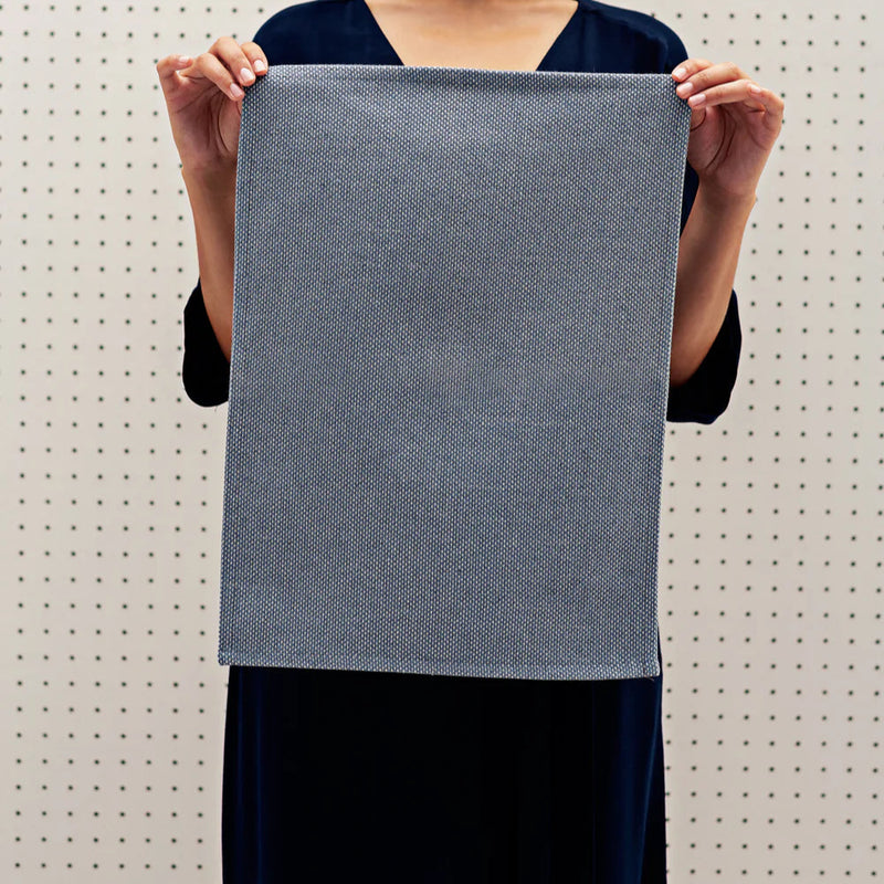 Person holding a large grey textured fabric swatch against a pegboard background.