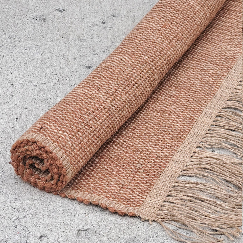 Rolled brown woven jute rug with tassel fringe on concrete background.