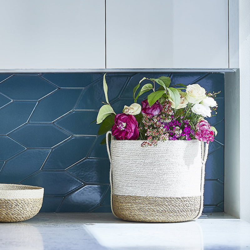 Decorative rope basket with vibrant flowers against a modern hexagon tile backsplash.