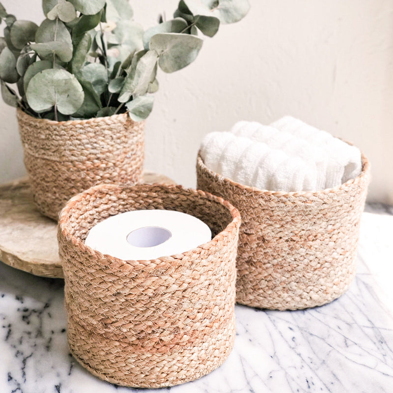 Natural woven baskets on marble surface containing toilet paper, towels, and eucalyptus plant for stylish bathroom organization.