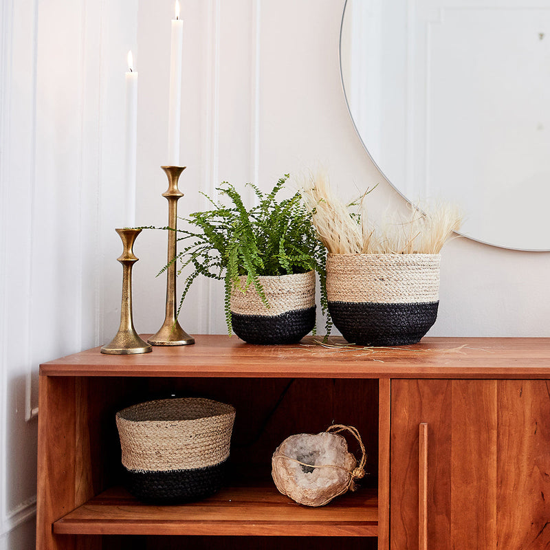 Elegant bohemian home decor with woven baskets, green plant, and brass candlesticks on a wooden console.