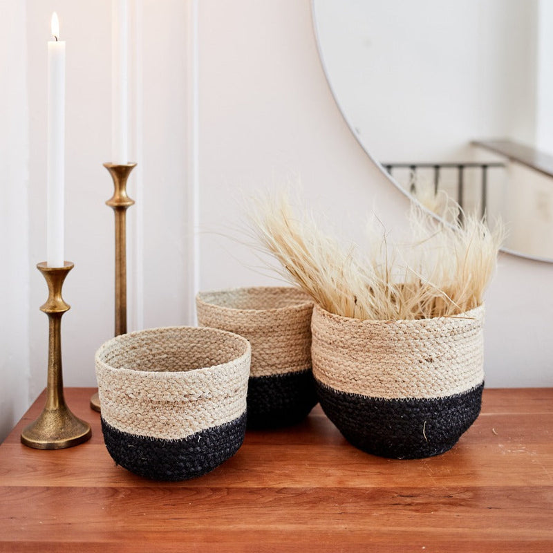 Handmade woven baskets with neutral tones on a wooden surface, styled with dried pampas grass near elegant brass candlesticks and a mirror.