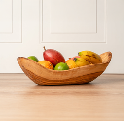 Wooden bowl filled with fresh fruit including bananas, oranges, limes, and a mango on a wooden table.