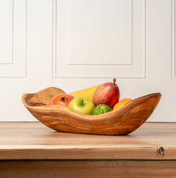 Wooden bowl filled with mixed fruit on a wooden table, featuring apples, pear, orange, lime, banana, and pomegranate.