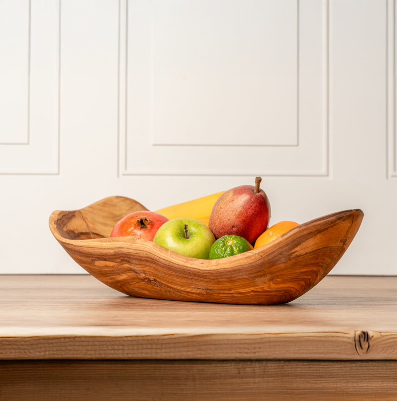 Wooden bowl filled with mixed fruit on a wooden table, featuring apples, pear, orange, lime, banana, and pomegranate.