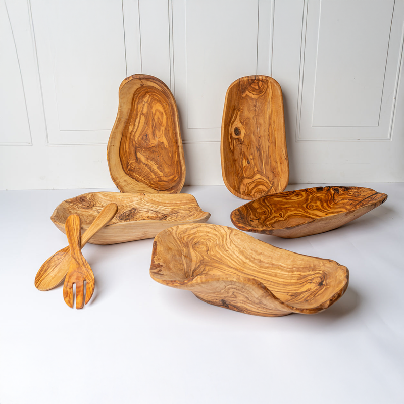 Handcrafted olive wood serving bowls and utensils set against a white textured wall background.