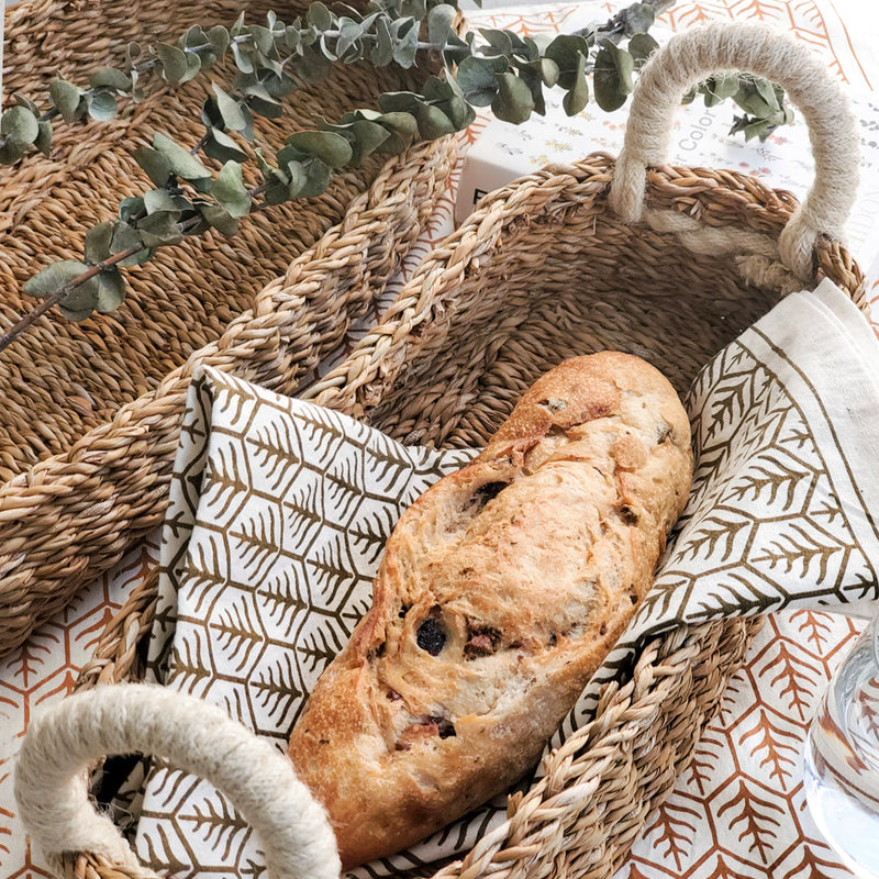 Rustic French baguette in woven basket with decorative cloth and eucalyptus branch.