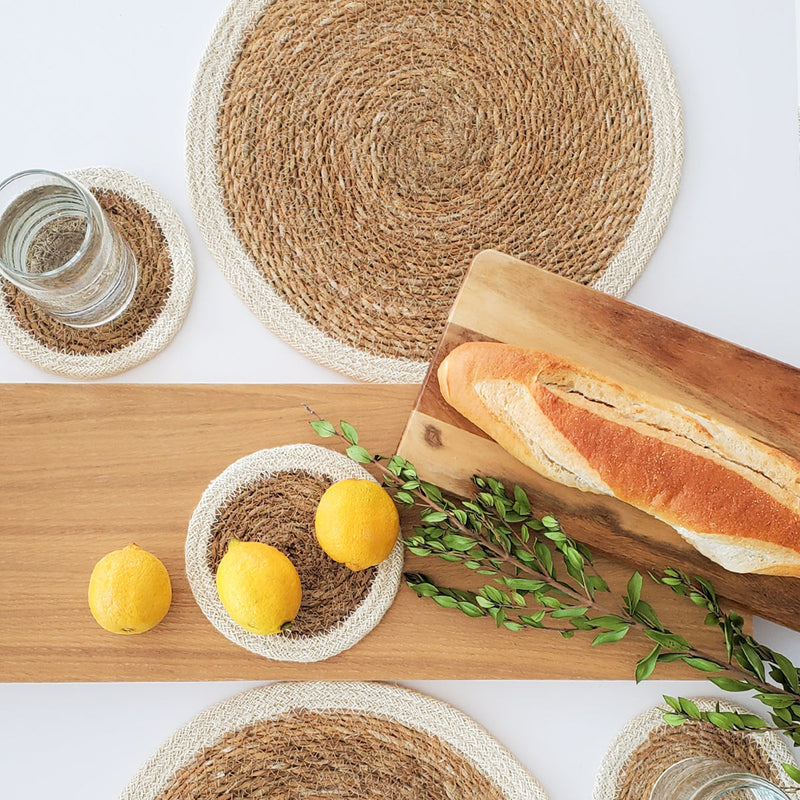 Rustic dining table setup with woven placemats, fresh lemons, bread on a wooden board, and greenery for a natural aesthetic.