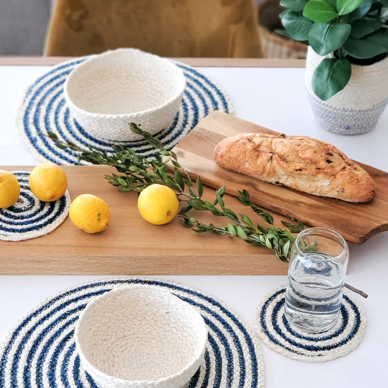 Rustic dining table setting with fresh lemons, baked bread, woven placemats, and houseplant for a cozy kitchen ambiance.
