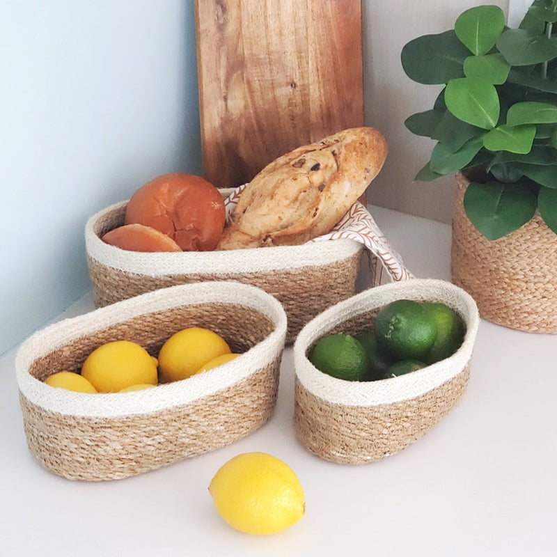 Woven baskets with lemons, limes, and bread on a white counter next to a potted plant.