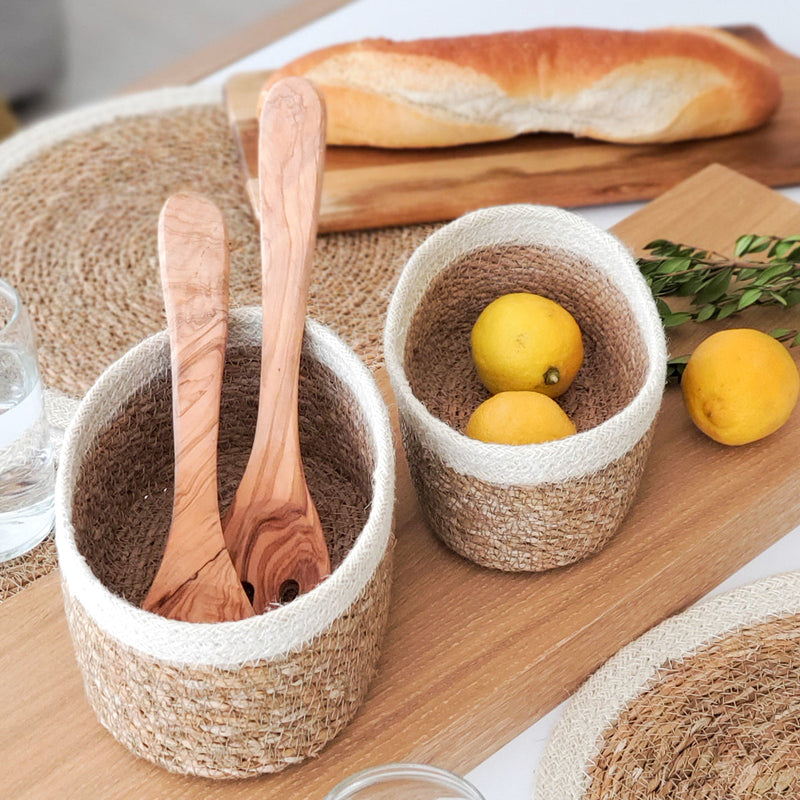 Woven baskets with lemons and wooden utensils on a rustic table setting, featuring a baguette in the background.