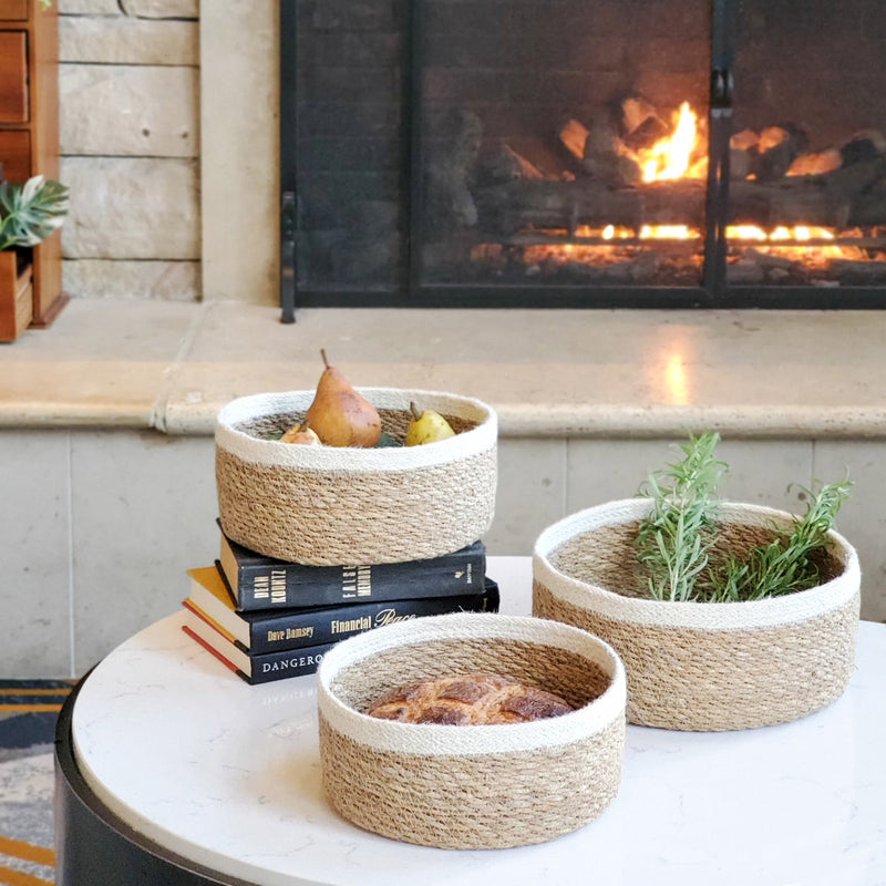 Rustic woven baskets with fruits and herbs on a table, cozy fireplace background.