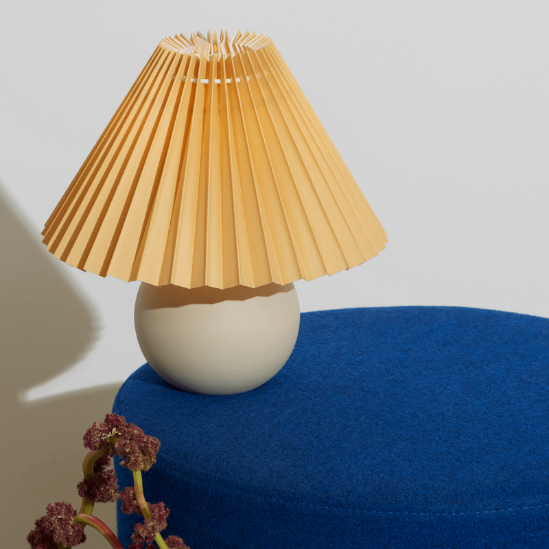 Contemporary table lamp with pleated shade on blue ottoman, modern home decor.